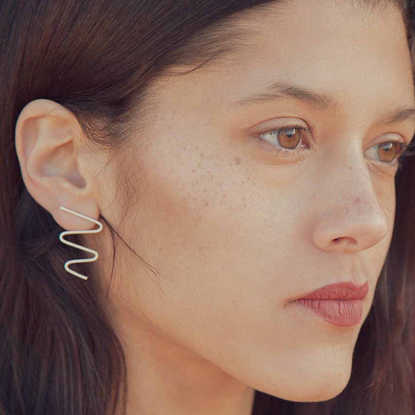 Primer plano de la modelo llevando los pendientes plateados con forma ondulada, de líneas suaves y diseño contemporáneo