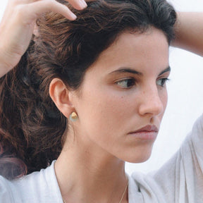 Pendientes con base dorada de forma orgánica y piedra semipreciosa Aqua calcedonia, ajustados al lóbulo de la oreja de la modelo.