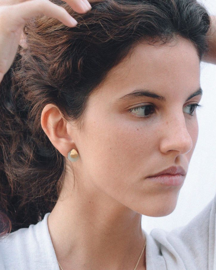 Pendientes con base dorada de forma orgánica y piedra semipreciosa Aqua calcedonia, ajustados al lóbulo de la oreja de la modelo.
