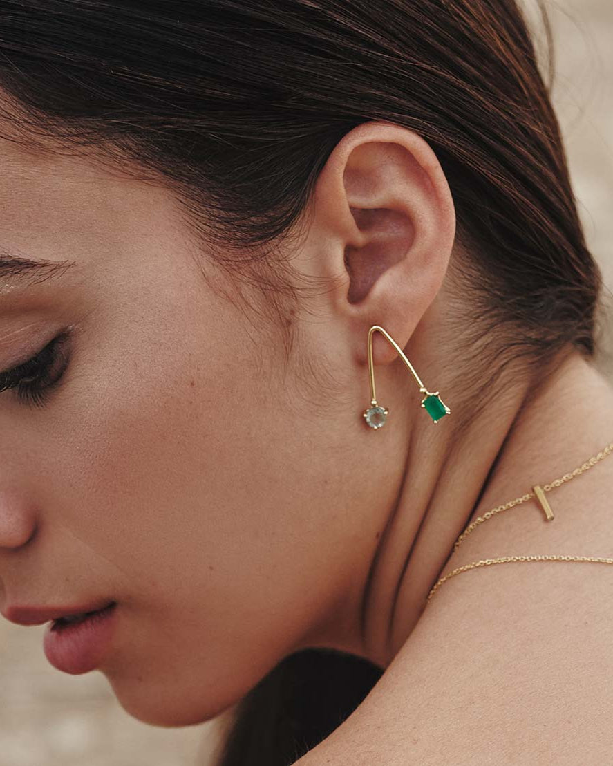 Modelo con pendientes artesanales de latón dorado con piedras ónix verde y amatista verde, y collares minimalistas dorados en capas. Conjunto de joyería elegante y moderno, ideal para ocasiones especiales o para el día a día.