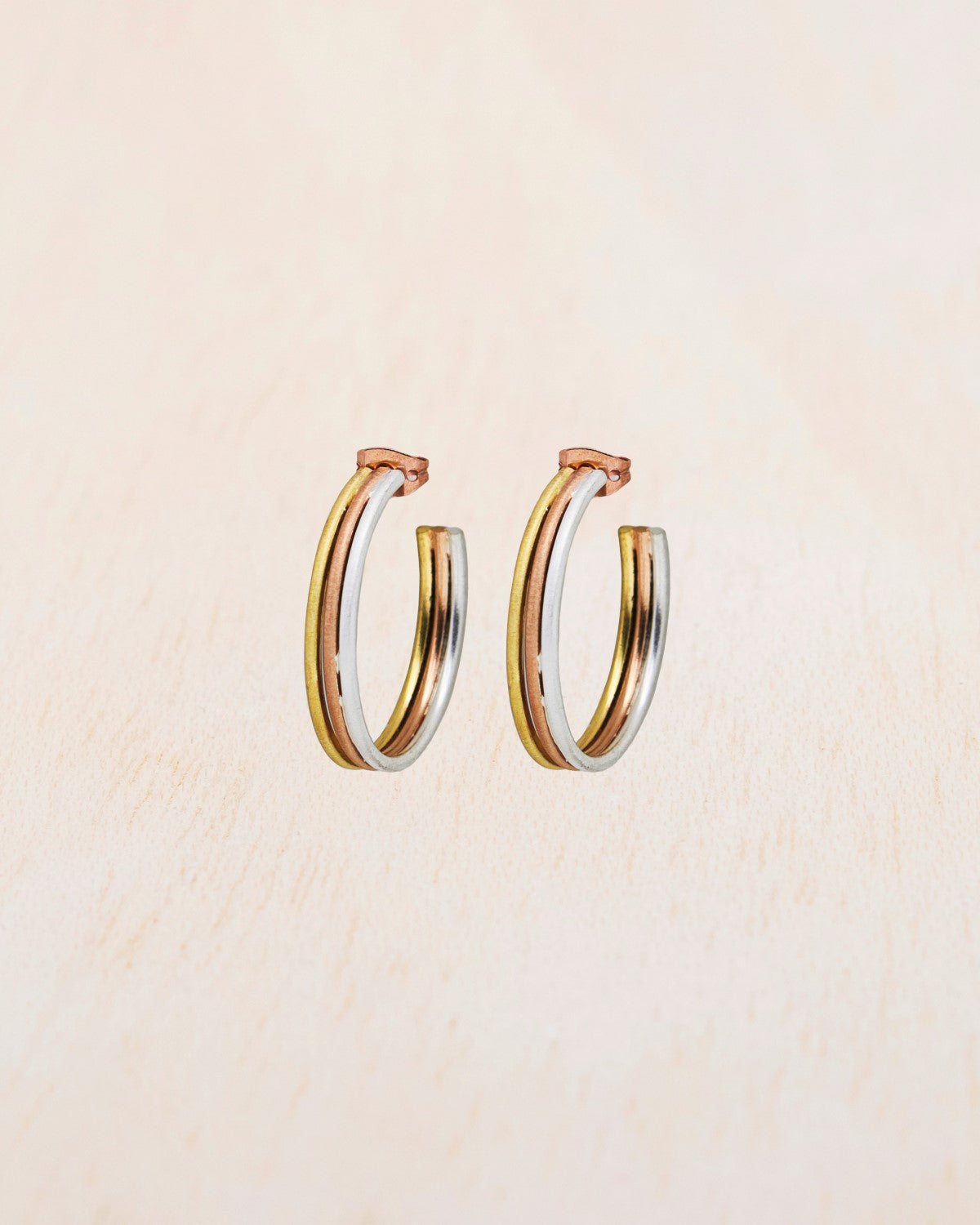 Aros tricolor de tamaño mediano con baño en oro 18k, oro rosa y plata 925 sobre fondo beige claro