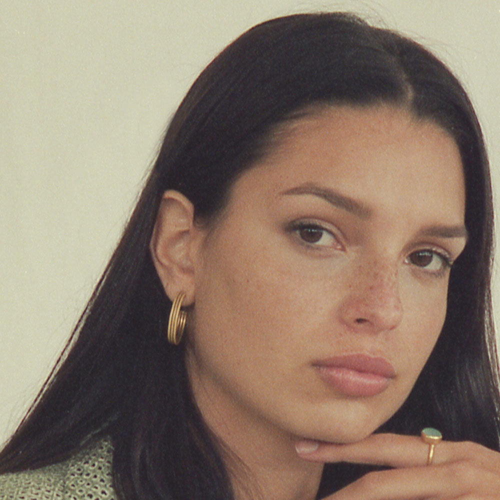 Primer plano de la modelo con cabello oscuro luciendo aros dorados medianos con diseño clásico y elegante