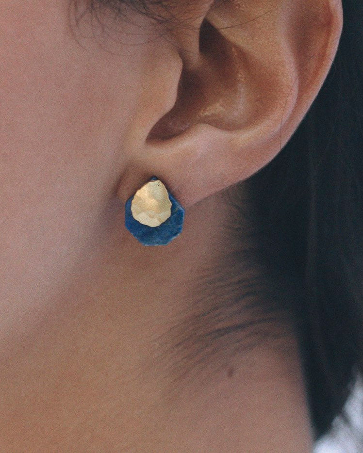 Pendientes pequeños de forma irregular con base en latón bañado en oro y piedra de lapislázuli, ajustados al lóbulo de la oreja.