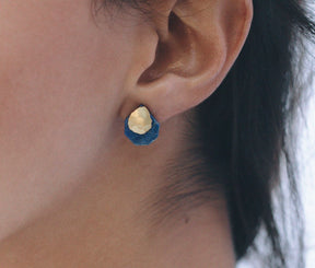 Pendientes pequeños de forma irregular con base en latón bañado en oro y piedra de lapislázuli, ajustados al lóbulo de la oreja.