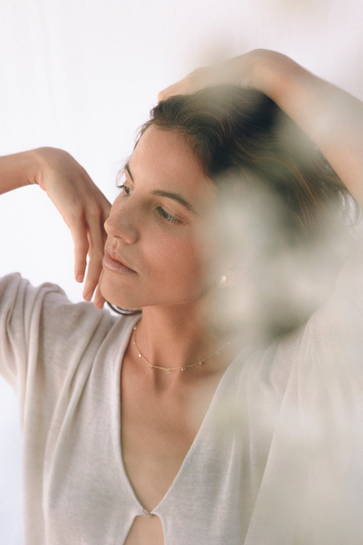 Pendiente pequeño de latón bañado en oro con piedra semipreciosa rosa engastada, llevado por una mujer con el cabello recogido y una blusa clara, en una escena suave y desenfocada.