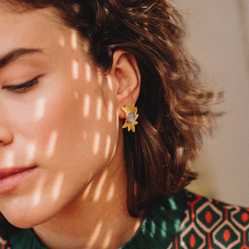pendientes dorados con diseño de hojas y piedra central en Piedra Luna en la oreja de la modelo bajo luz natural