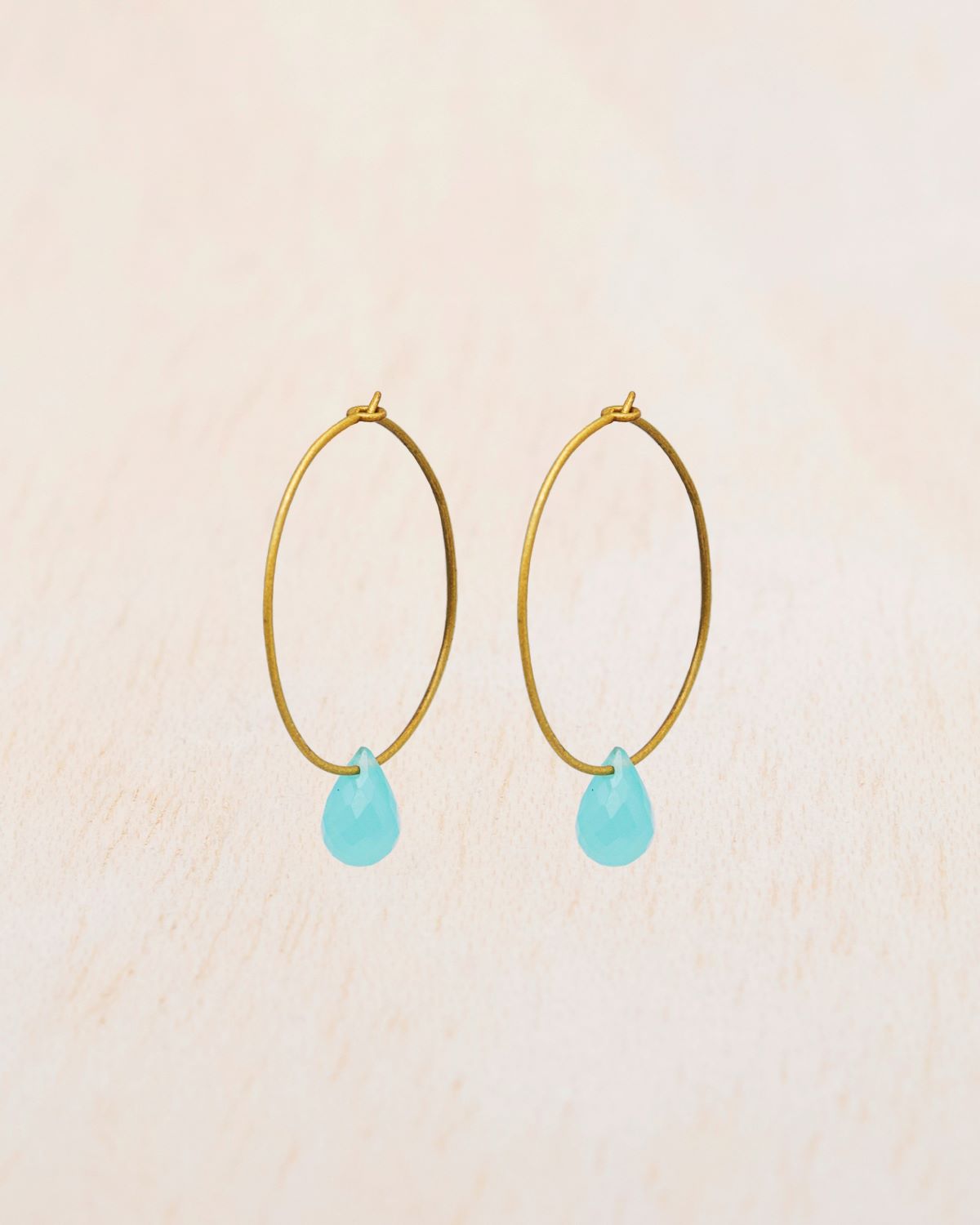 Primer plano de los pendientes en forma de Aro bañado en oro de 18 quilates con piedra semipreciosa Aqua Calcedonia en forma de gota