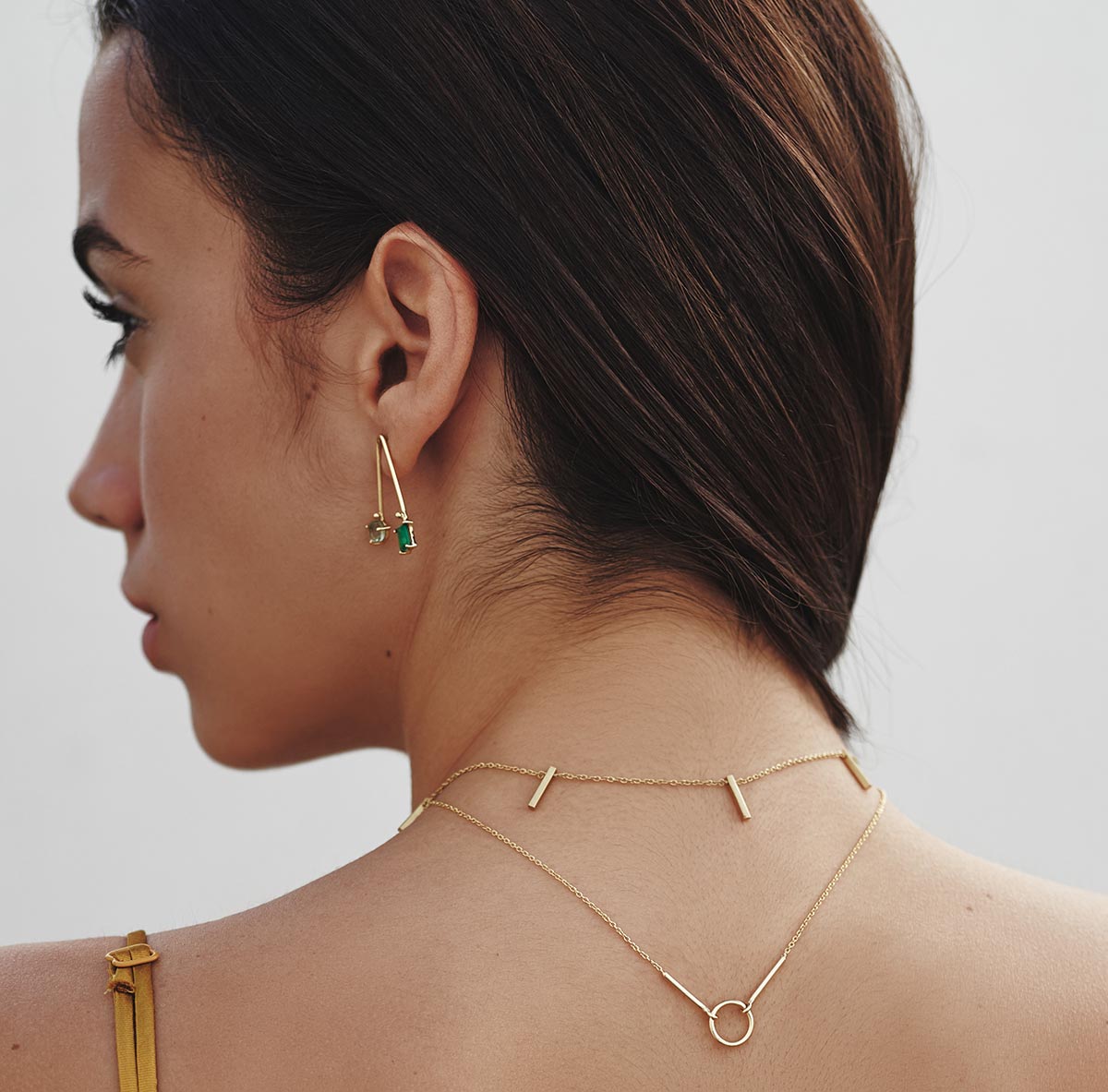 Mujer con pendientes colgantes artesanales de latón dorado con piedras verdes esmeralda. Diseño elegante y minimalista, perfecto para ocasiones especiales o para un look sofisticado diario.