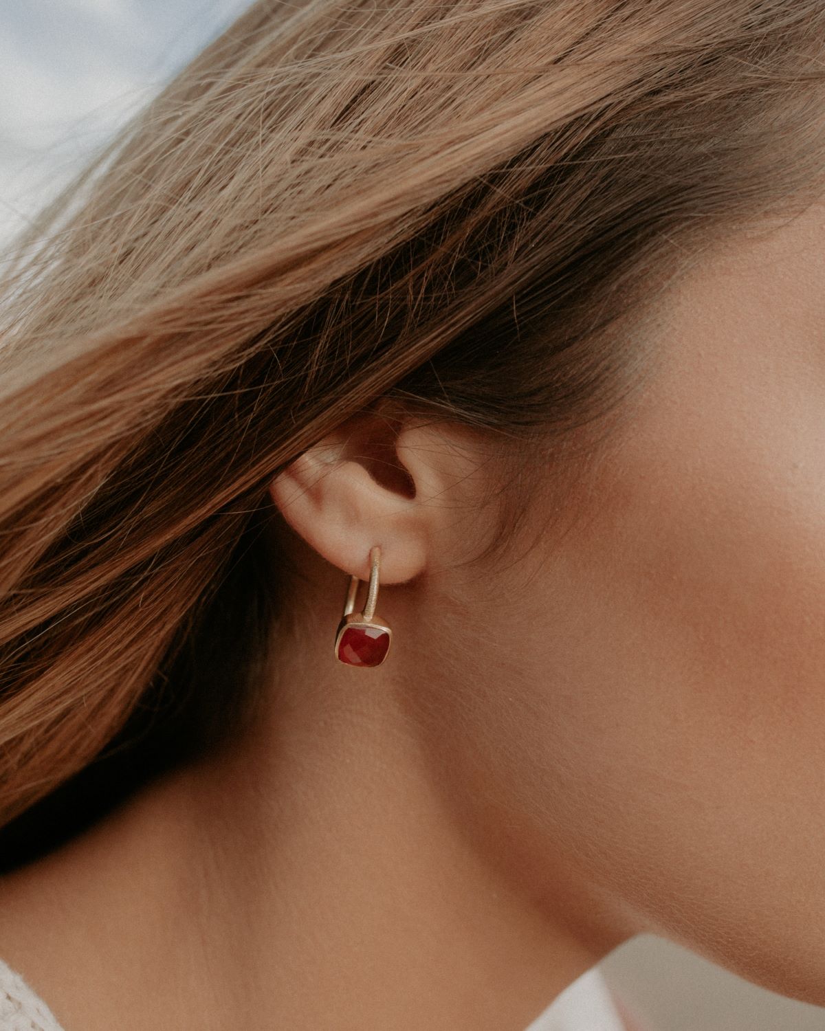 Primer plano de la modelo con los pendientes bañados en Oro de 18 quilates con piedra tallada de forma cuadrada en Cornalina de Isla Vurma