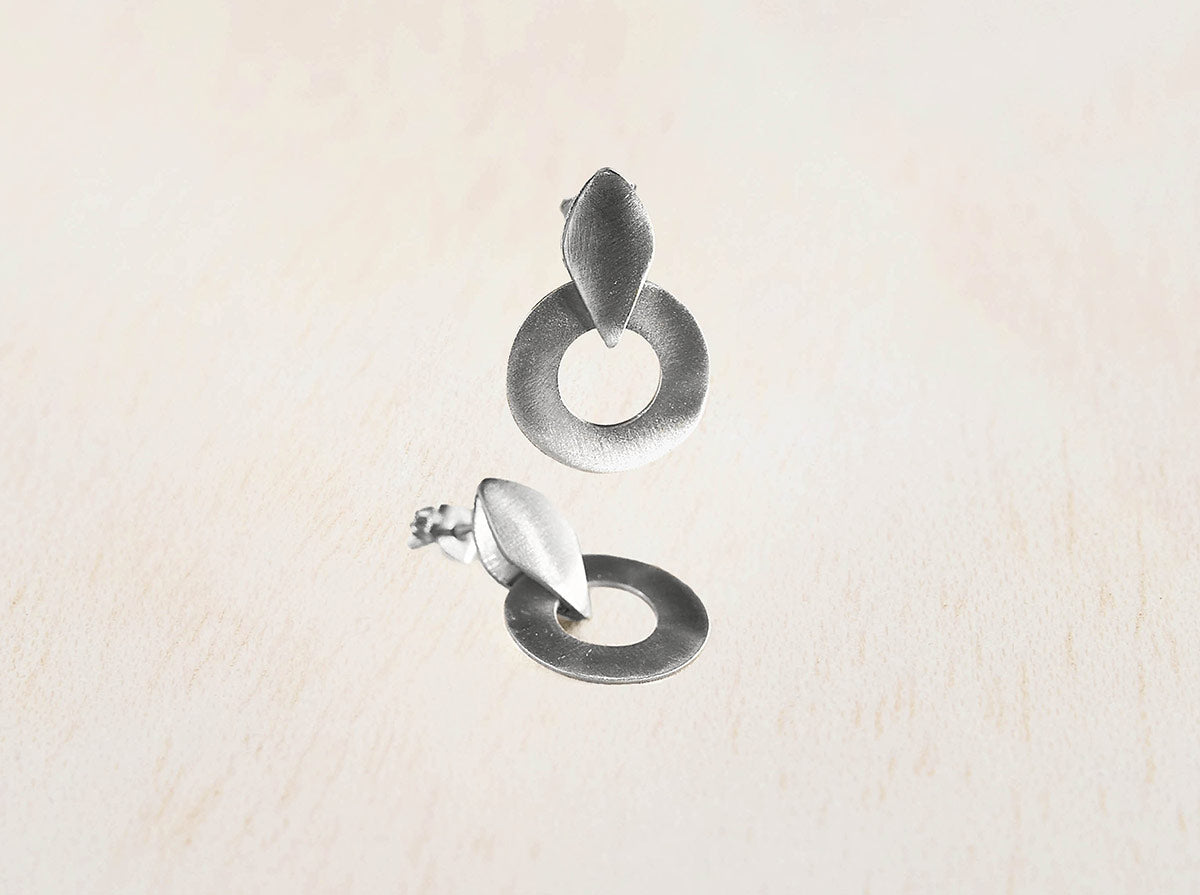 Pendientes de aro circular con forma de hoja superior, elaborados en plata 925 con acabado mate, sobre fondo beige claro