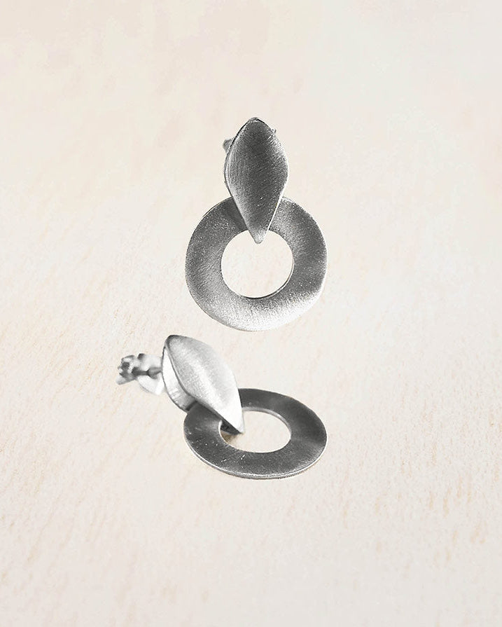 Pendientes de aro circular con forma de hoja superior, elaborados en plata 925 con acabado mate, sobre fondo beige claro