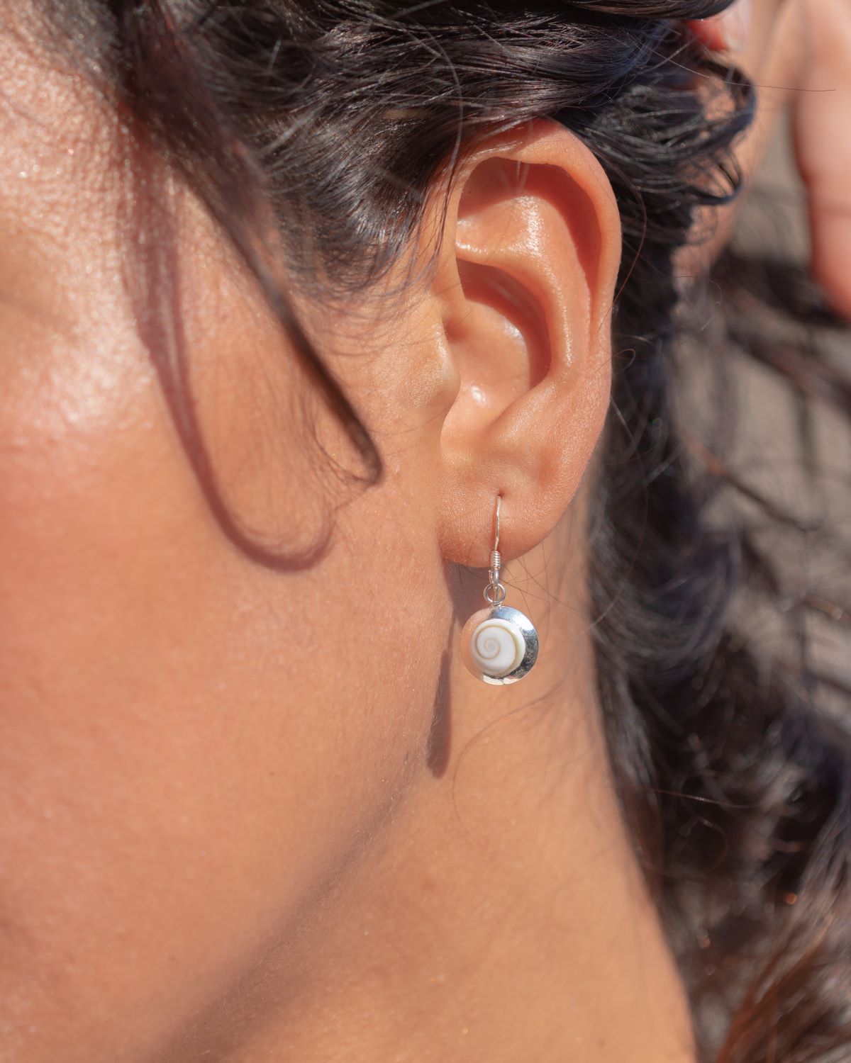 Pendientes puestos sobre oreja pequeños artesanales de Ojo de Santa Lucía montados en plata de ley 925 con diseño en espiral sobre fondo beige claro

