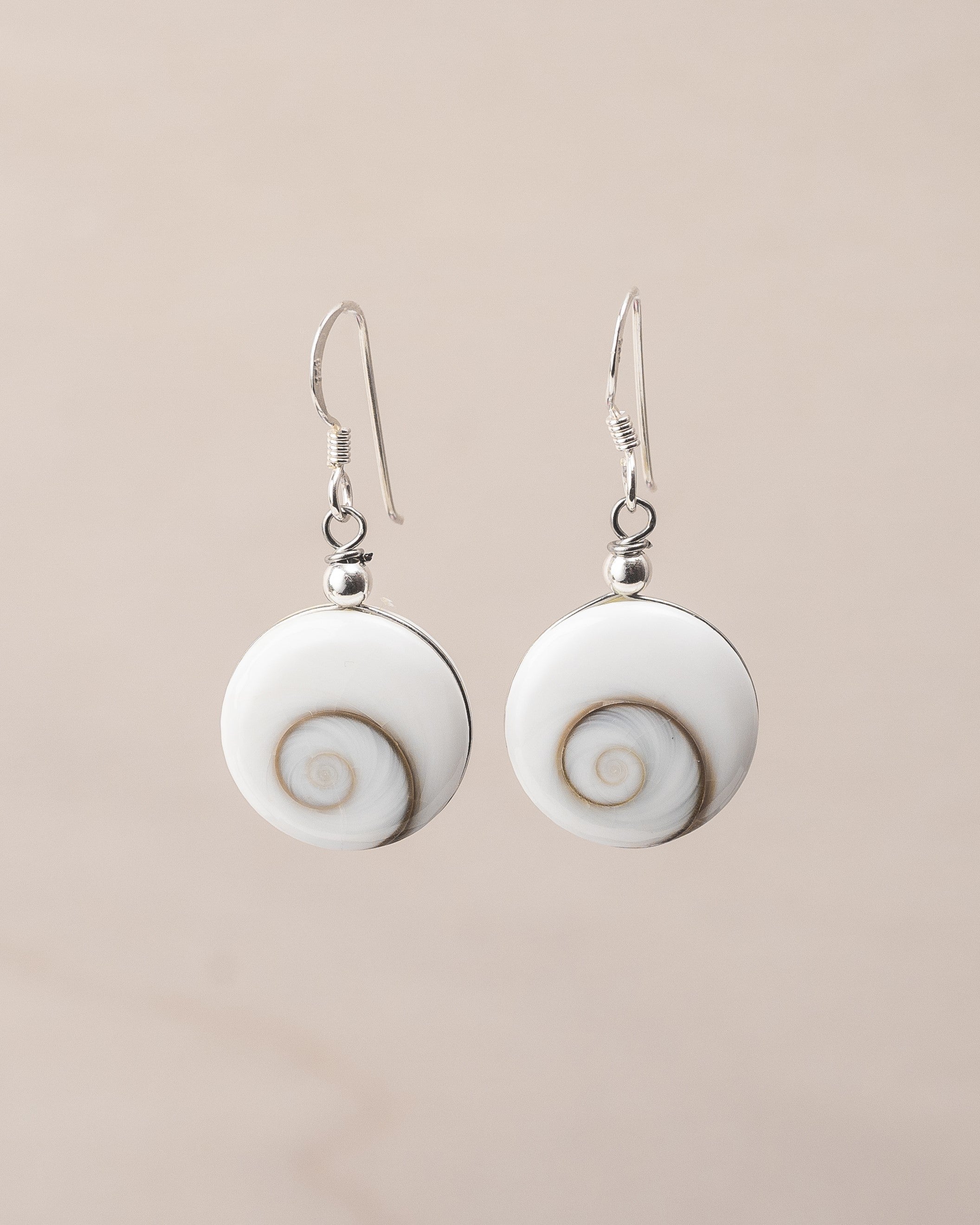 Pendientes artesanales de plata de ley con Ojo de Santa Lucía. Concha formada por espiral natural y montura de plata de ley sobre fondo neutro