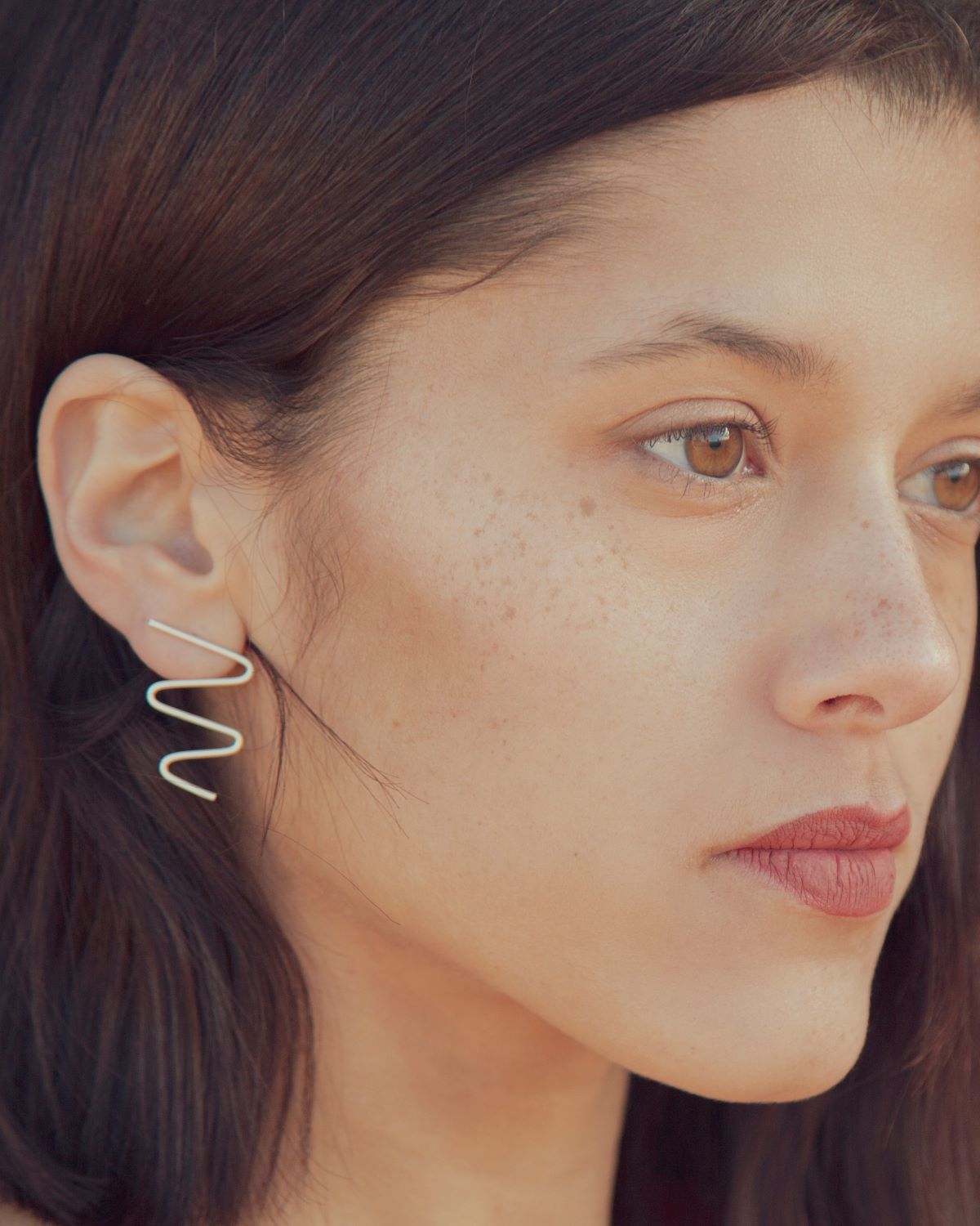 Primer plano de la modelo luciendo los pendientes plateados con forma ondulada, elaborado latón bañados en Plata de Ley 925