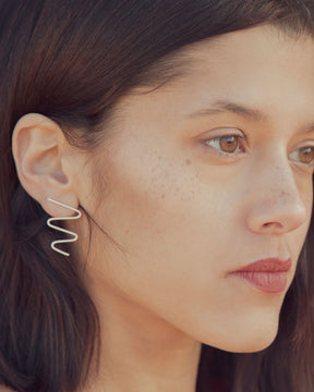 Primer plano de la modelo luciendo los pendientes plateados con forma ondulada, elaborado latón bañados en Plata de Ley 925