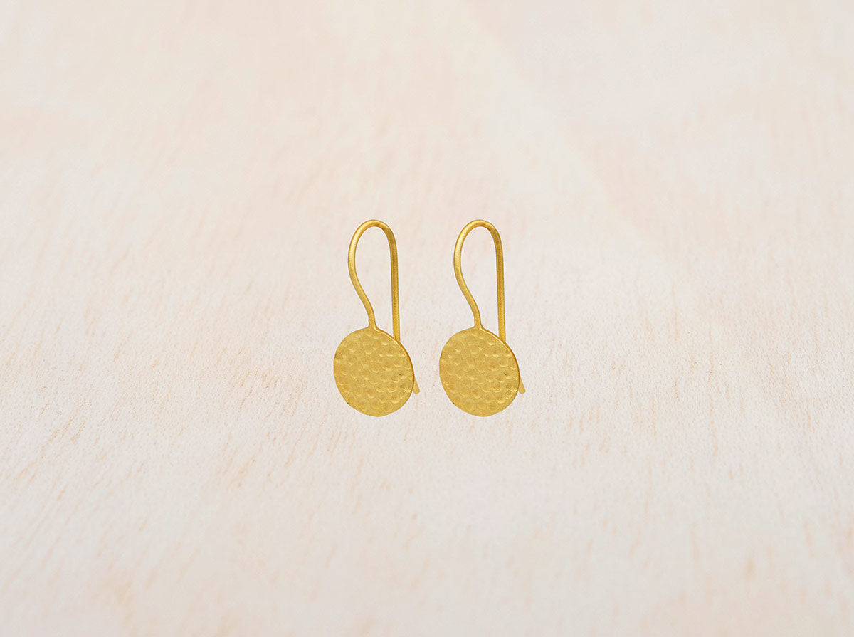 Pendientes circulares de latón bañados en oro de 18 quilates con textura martillada sobre fondo beige claro