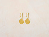 Pendientes circulares de latón bañados en oro de 18 quilates con textura martillada sobre fondo beige claro