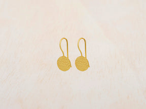 Pendientes circulares de latón bañados en oro de 18 quilates con textura martillada sobre fondo beige claro