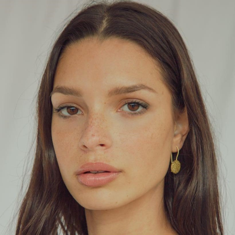 Modelo con pendientes circulares dorados con textura martillada en baño de oro 18 quilates. Fondo claro