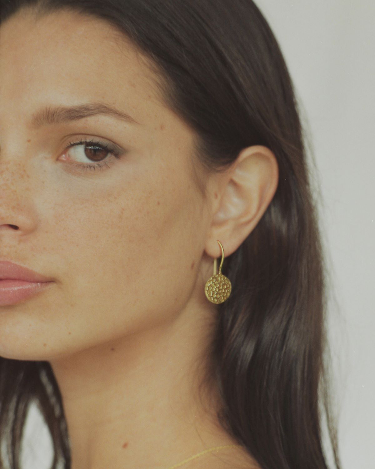 Medio plano de la modelo con pendientes dorados redondos con textura martillada, bañado en oro de 18 quilates 