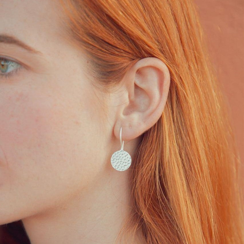 Modelo pelirroja con pendientes largos bañados en plata, redondos con textura martillada