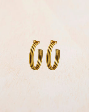 Aros dorados gruesos de acabado pulido sobre fondo beige claro