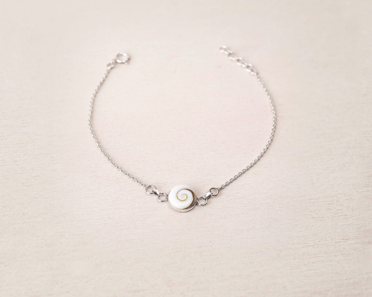 Pulsera plateada con concha natural de Santa Lucía sobre fondo beig