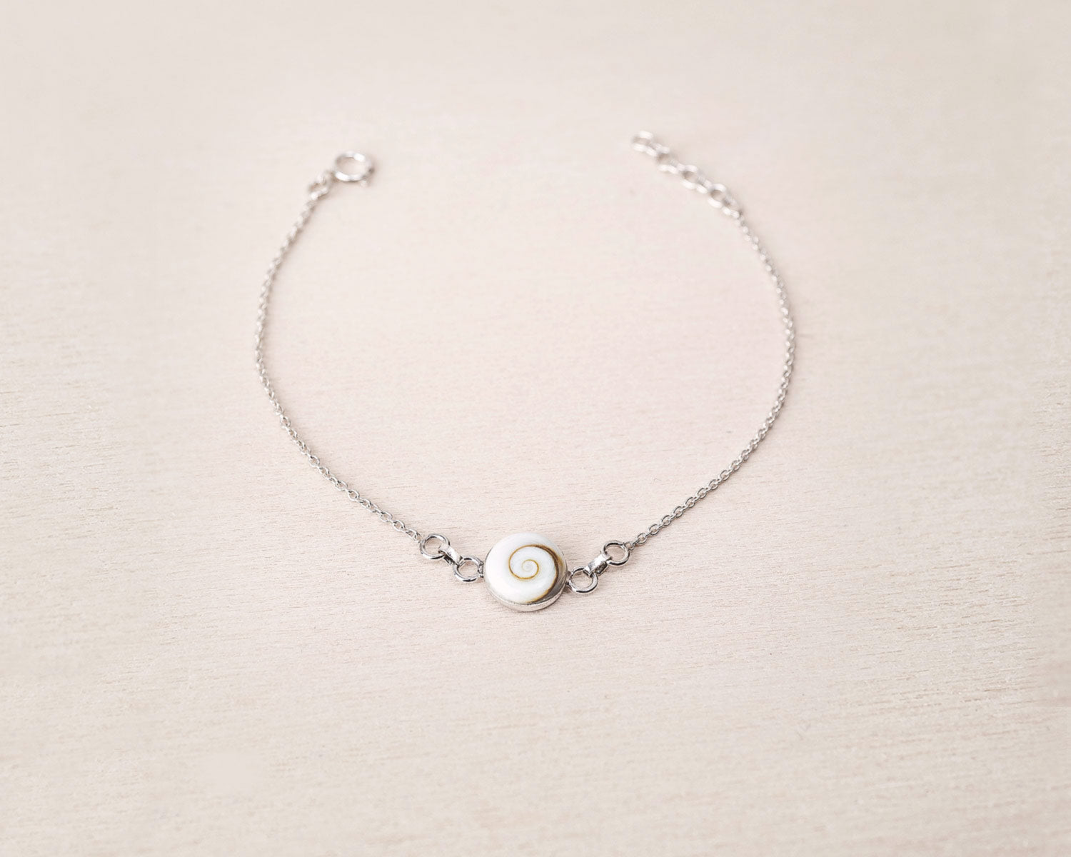 Pulsera plateada con concha natural de Santa Lucía sobre fondo beig