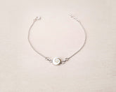 Pulsera plateada con concha natural de Santa Lucía sobre fondo beig