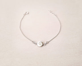 Pulsera plateada con concha natural de Santa Lucía sobre fondo beig