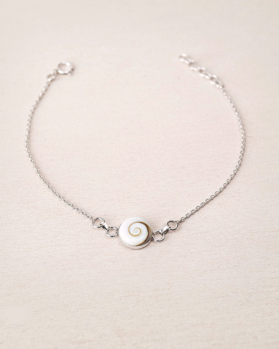 Pulsera plateada con concha natural de Santa Lucía sobre fondo beig