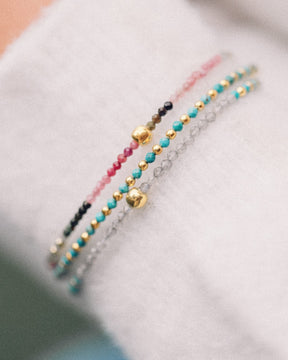 Primer plano de un conjunto compuesto por tres pulseras con cuentas facetadas de piedra semipreciosa en Aqua Calcedonia, Turmalina Multicolor, Labradorita y bañadas en Oro de 18 quilates