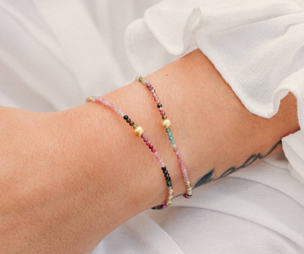 Primer plano de un conjunto compuesto por dos pulseras con cuentas facetadas de piedra semipreciosa en Turmalina Multicolor y bañadas en Oro de 18 quilates