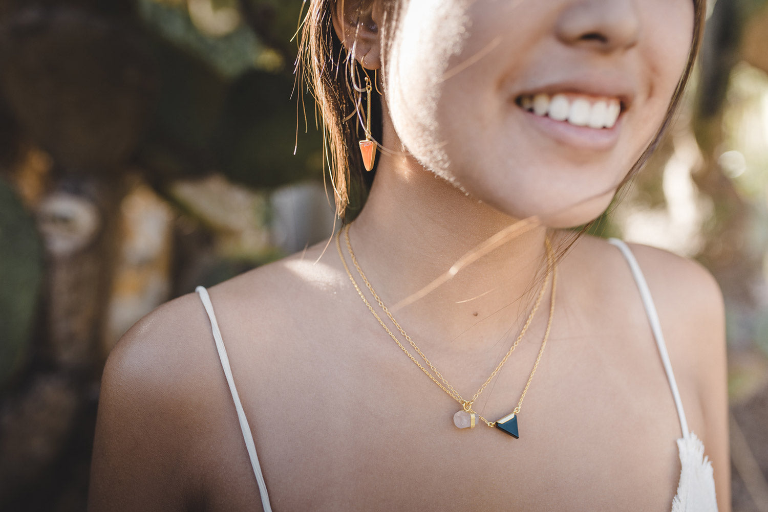 Modelo con conjunto de collares bañados en oro de 18 quilates con piedra semipreciosa de Cuarzo Rosa sujeta por una pequeña pieza dorada y una pequeña pieza triangular negra, además de unos pendientes en forma triangular dorados de Isla Vurma