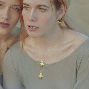 Plano de dos modelos mirando al frente luciendo los pendientes dorados con forma ondulada, elaborado en metal acabado satinado