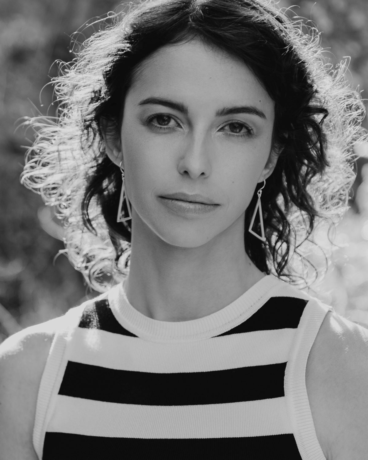 Mujer con pendientes triangulares de plata 925 y top de rayas blancas y negras, iluminada por luz natural.