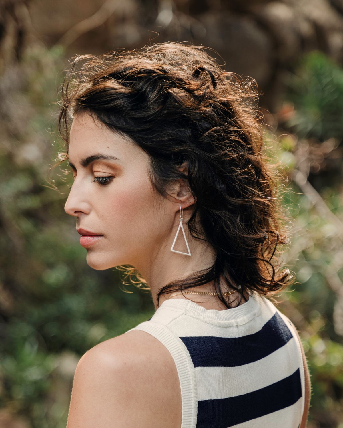 Pendientes triangulares plateados lucidos por la modelo en perfil, con fondo natural y luz suave.